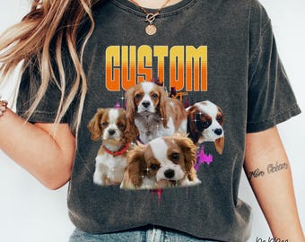 Könnte beinhalten: Ein dunkelgraues T-Shirt mit einer Retro-Grafik von vier Cavalier King Charles Spaniels. Die Grafik zeigt das Wort "CUSTOM" in einer fetten, orangen Schrift mit gelbem Umriss. Die Hunde sind in einer verspielten Pose angeordnet, mit geneigten Köpfen und herausgestreckten Zungen. Die Grafik ist von einem farbenfrohen, abstrakten Design umgeben.