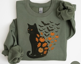 Puede incluir: Sudadera verde militar con un gato negro de ojos naranjas, rodeado de murciélagos, calabazas y hojas de otoño. El gato está adornado con diseños temáticos de otoño. Una cómoda parte superior de manga larga, perfecta para Halloween o el otoño.