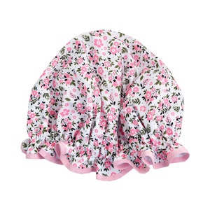 May include: A white shower cap with a pink and green floral pattern. The cap has a pink ruffled edge.