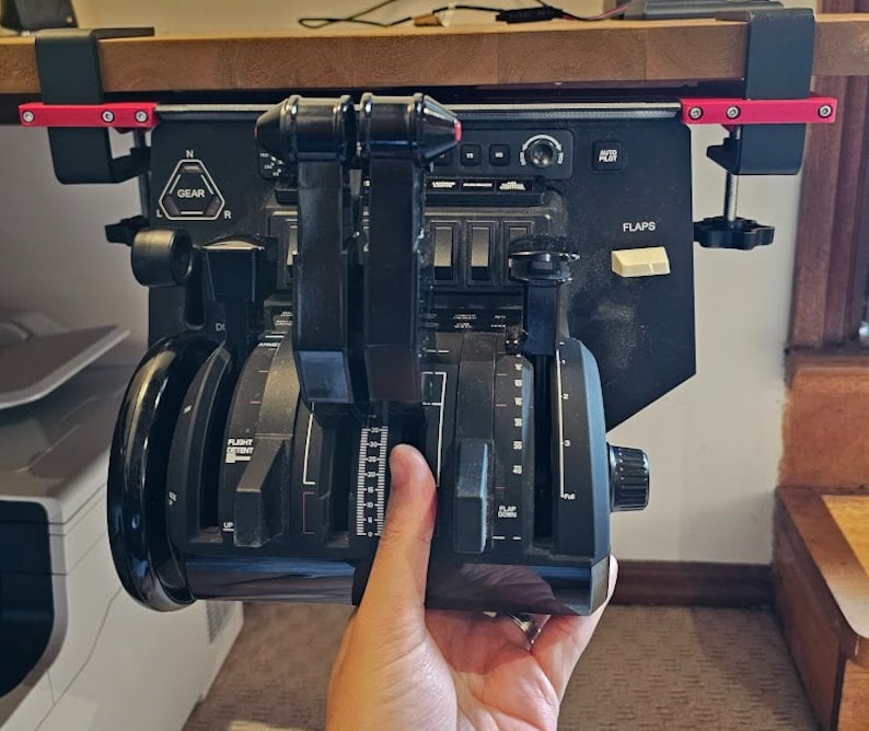 May include: Black flight simulator throttle quadrant with multiple levers, dials, and switches. The unit is mounted to a wooden surface with red and black clamps. The word "GEAR" is visible on the panel.