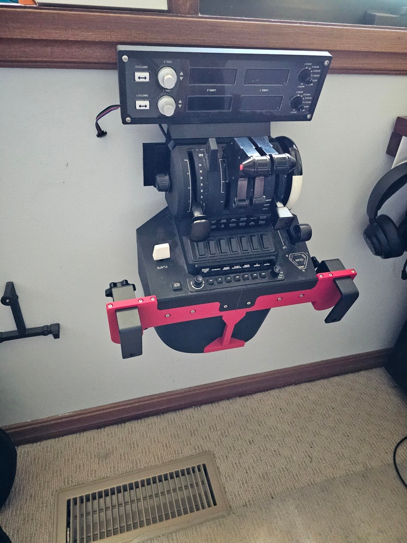 May include: Black and red flight simulator control panel mounted on a wall. The panel features various dials, switches, and levers, with a digital display. The unit is designed for flight simulation and training purposes.