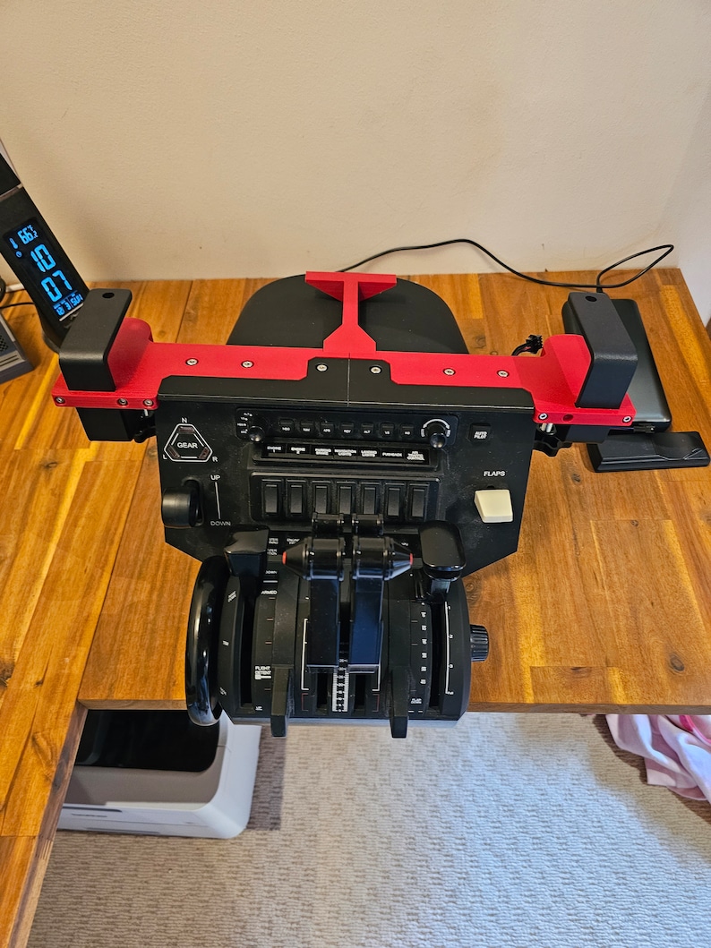 May include: A black and red flight simulator control panel with multiple levers, switches, and dials. The panel has a digital display and is mounted on a wooden surface. The gear and flaps controls are visible.