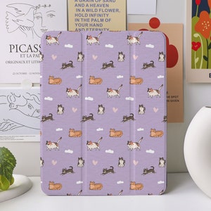 May include: Purple iPad case with a repeating pattern of white clouds, pink hearts, and orange, white, and black cats. The case has a textured surface.