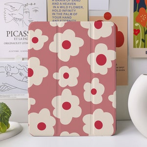 Pode incluir: Uma capa para iPad rosa com um padrão floral branco. As flores têm centros vermelhos e estão dispostas em um padrão repetitivo.