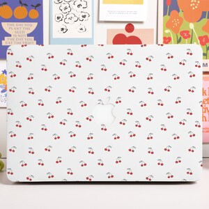 Può includere: Un computer portatile bianco con un motivo a ciliegie sul coperchio. Il computer portatile ha un logo Apple argentato sul coperchio.