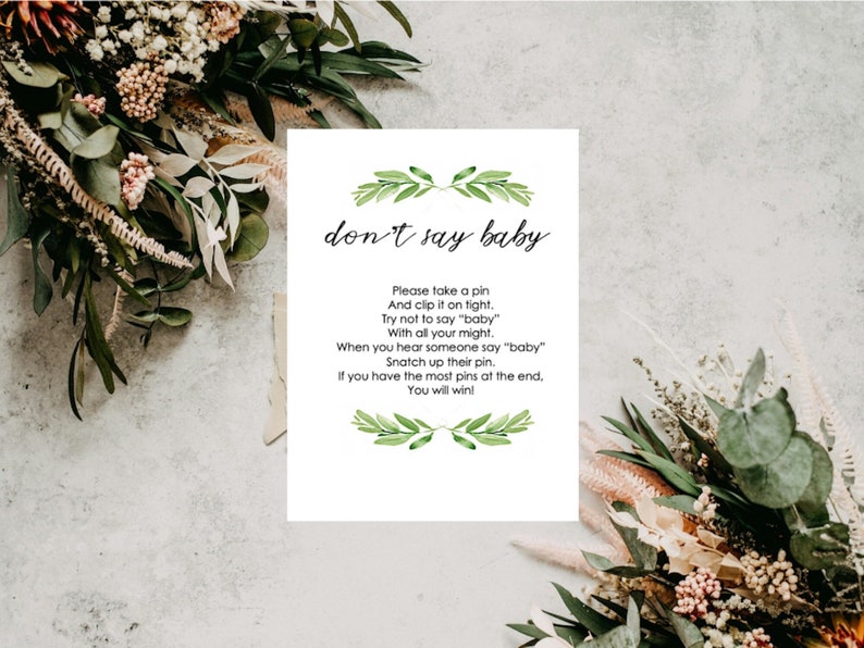 Puede incluir: Una tarjeta blanca con el texto "don't say baby" en escritura negra, con un dise&ntilde;o de hojas verdes. La tarjeta incluye instrucciones para un juego de baby shower. La tarjeta est&aacute; rodeada de arreglos florales.
