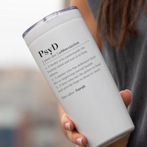 May include: White travel mug with a black and white definition of "PsyD" printed on the side. The definition reads: "[psce-dee | abbreviation 1. A healer who understands the human mind and uses it to help others. 2. A master who has dedicated their life to improving mental health. 3. A hero who has the power to heal and provide hope to those in need. See also: Sarah"