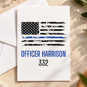 May include: A white rectangular greeting card featuring a distressed black and white American flag graphic with a single horizontal blue stripe. Below the flag, the text reads OFFICER HARRISON in blue and the number 332 in black.
