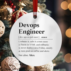 May include: A round white ceramic ornament hanging from a red ribbon. The text reads: Devops Engineer [dev-ops en-juh-neer] noun 1. reboots it, calls it a root cause 2. fluent in YAML and rollbacks 3. never deploys on a Friday, mostly 4. runs prod on coffee and alerts See also: Alex