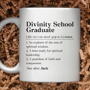 May include: White ceramic mug with a black design that defines "Divinity School Graduate" as an explorer of spiritual wisdom, a hero ready for spiritual leadership, and a guardian of faith and compassion. The mug also says "See also: Jack".
