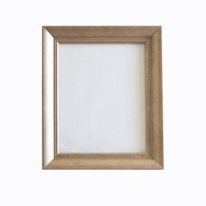 Puede incluir: Un marco de fotos rectangular con acabado dorado. El marco tiene un diseño simple y clásico con una superficie ligeramente texturizada. El interior del marco es blanco, listo para una fotografía o una obra de arte. El marco es adecuado para exhibir varios tipos de imágenes.