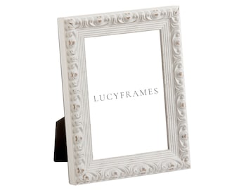 May include: White ornate picture frame with a distressed finish. The frame is standing upright on a white surface. The text "LUCYFRAMES" is visible in the center of the frame.