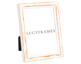 May include: White picture frame with a distressed, weathered look and a light orange border. The frame is standing on a white surface. The text "LUCYFRAMES" is printed on the frame.