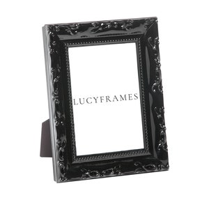 Puede incluir: Marco de fotos negro adornado con un diseño decorativo. El marco está hecho de plástico y tiene un acabado brillante. El marco está de pie sobre un fondo blanco. El texto "LUCYFRAMES" es visible en el marco.