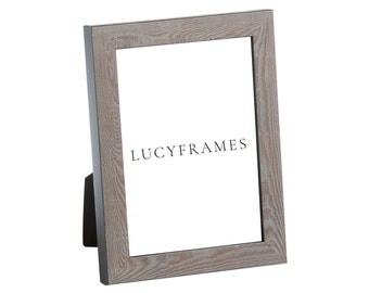 May include: A light gray wood picture frame with a whitewashed finish. The frame has a simple design and is perfect for displaying photos or artwork. The frame is made of wood and has a matte finish. The frame is standing on a white surface. The text "LUCYFRAMES" is printed on the frame.