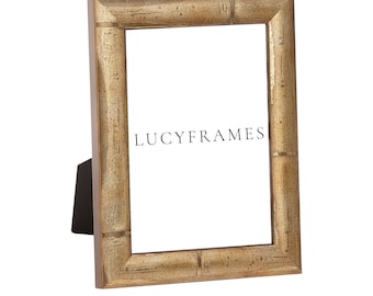 May include: A gold-toned picture frame with a textured, wood-like finish. The frame is standing on a white surface. The text "LUCYFRAMES" is printed on the frame.