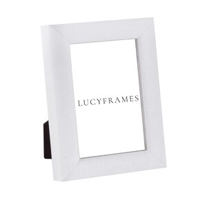 May include: White picture frame with a textured surface and a beveled edge. The frame is standing upright on a white surface. The text "LUCYFRAMES" is printed on the frame.