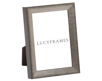 May include: A silver picture frame with a wood grain finish. The frame is standing upright on a white background. The text "LUCYFRAMES" is printed on the frame.