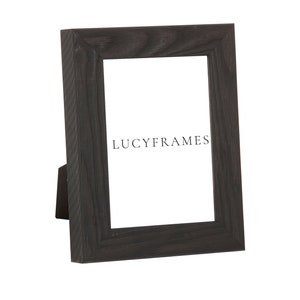 May include: A black wooden picture frame with a stand on the back. The frame has a simple design and is made of dark wood with a slightly textured finish. The frame is empty and ready to display a photo or artwork. The text "LUCYFRAMES" is printed on the frame.