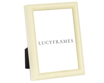May include: A cream-colored picture frame with a textured surface. The frame is made of wood and has a simple design. The frame is sitting on a white background. LUCYFRAMES is printed on the frame.