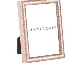 May include: A rose gold hammered metal picture frame with a white mat and the text "LUCYFRAMES" printed on the mat.