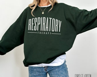 May include: Forest green sweatshirt with the words "RESPIRATORY THERAPY" in white block letters. The sweatshirt is a dark green color and has a relaxed fit. The text "FOREST GREEN" is written in a script font in the bottom right corner.