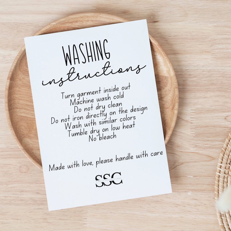 May include: A white card with black text outlining washing instructions for a garment. The text reads: "WASHING instructions Turn garment inside out Machine wash cold Do not dry clean Do not iron directly on the design Wash with similar colors Tumble dry on low heat No bleach Made with love, please handle with care SSC"