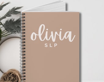 May include: A beige spiral bound notebook with the name "olivia SLP" written in white cursive on the front cover.