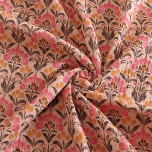 May include: Close-up of a floral fabric with a repeating pattern of pink and orange flowers, dark brown stems, and leaves on a cream background. The fabric is gathered, showing the texture and folds of the material.