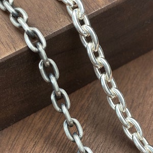 May include: Two silver chains, one with a polished finish and the other with a darker, oxidized finish, are displayed on a wooden surface.