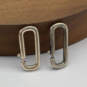 May include: A pair of silver oval-shaped earrings with a hook closure.