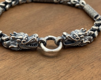 May include: A silver bracelet with two dragon head charms and a round clasp. The bracelet is made of a chain link design.