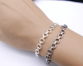 Puede incluir: Dos pulseras de cadena plateadas con eslabones circulares se muestran en la muñeca de una persona. Las pulseras están hechas de un material metálico brillante y están colocadas una al lado de la otra. El fondo es una superficie blanca lisa.