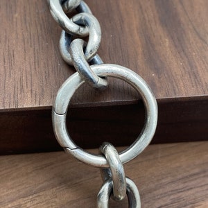 Könnte beinhalten: Nahaufnahme einer silbernen Kette mit einem großen, runden Glied. Die Kette ist aus dickem, schwerem Metall gefertigt und hat eine polierte Oberfläche.