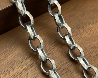 May include: A silver chain necklace with a textured, faceted link design. The chain is lying on a wooden surface.