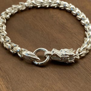 以下が含まれることがあります： ドラゴンヘッドクラスプ付きのシルバーブレスレット。ブレスレットはチェーンリンクのデザインで作られています。