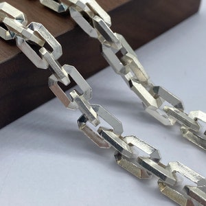 Puede incluir: Un collar de cadena de plata con un diseño de cadena de caja. La cadena está hecha de eslabones entrelazados que tienen forma rectangular.