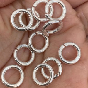 May include: A close-up of a pile of silver jump rings. The rings are all the same size and are arranged in a random pattern.
