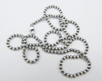 May include: A silver beaded necklace with a lobster clasp. The necklace is composed of small, round beads strung together, creating a textured and elegant accessory. The beads are a muted silver color.