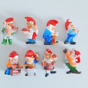 Pode incluir: Conjunto de oito figuras em miniatura de gnomos com chapéus vermelhos e roupas variadas. Os gnomos estão segurando ferramentas, comida e outros objetos.