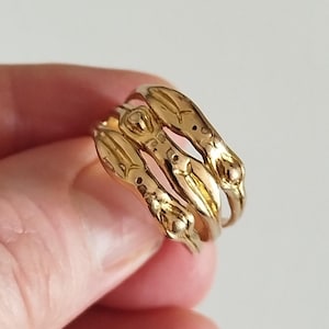 May include: A set of three stacked gold rings featuring an organic, irregular band design with raised, rounded nodes and subtle etched markings along the surface of each individual band, creating a textured and layered appearance on the finger.