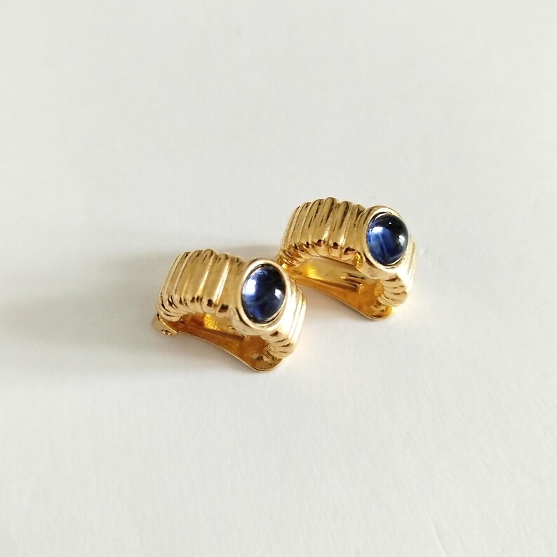 K&ouml;nnte beinhalten: Ein Paar goldfarbene Ohrclips mit blauen ovalen Steinen.