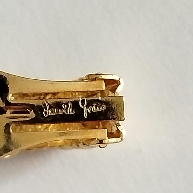 K&ouml;nnte beinhalten: Nahaufnahme einer goldfarbenen Metallschlie&szlig;e mit der Aufschrift "David Yurman" auf der R&uuml;ckseite.