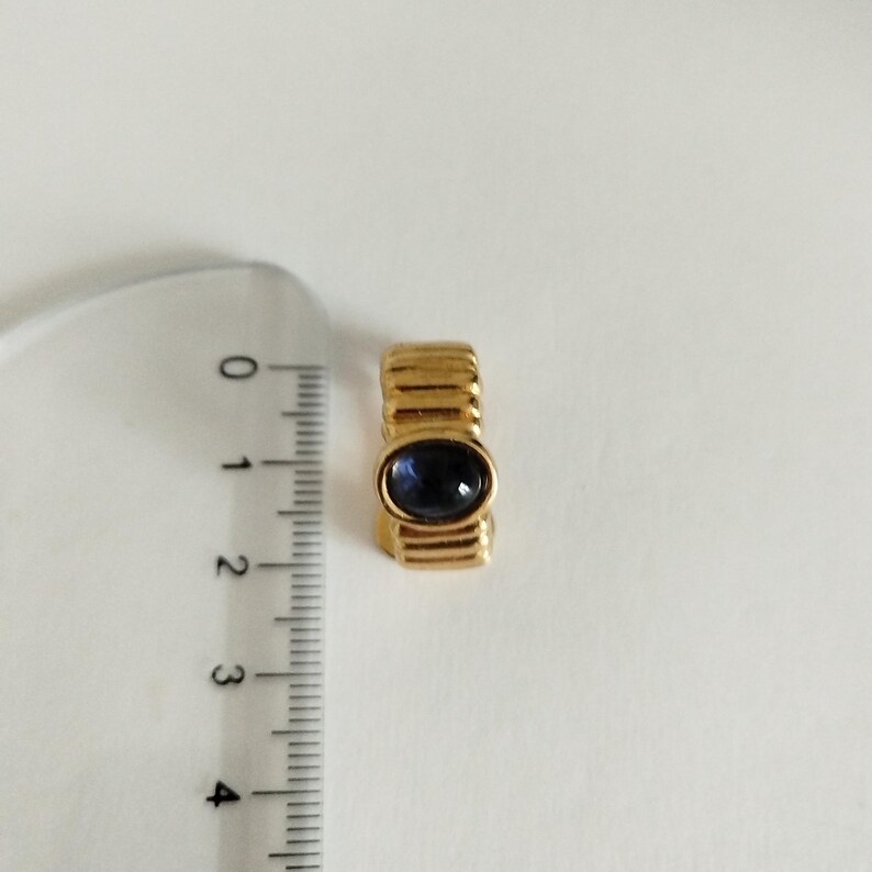 K&ouml;nnte beinhalten: Ein goldener Ring mit einem blauen, ovalen Edelstein. Der Ring hat eine strukturierte Band.