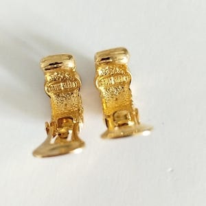 K&ouml;nnte beinhalten: Ein Paar goldfarbene Creolen mit einem strukturierten Design. Die Ohrringe haben einen Clipverschluss und sind auf der R&uuml;ckseite mit "David Yurman" gekennzeichnet.