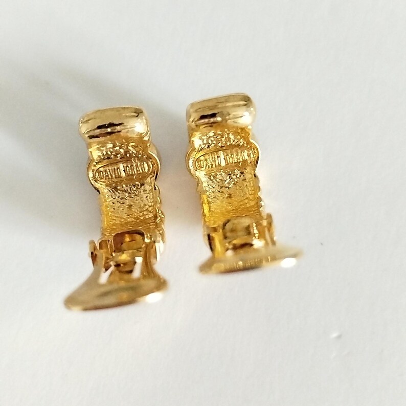 K&ouml;nnte beinhalten: Ein Paar goldfarbene Creolen mit einem strukturierten Design. Die Ohrringe haben einen Clipverschluss und sind auf der R&uuml;ckseite mit "David Yurman" gekennzeichnet.