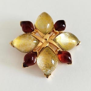 Könnte beinhalten: Eine sternförmige Brosche mit einem goldfarbenen Metallrahmen, der vier große, durchscheinende, gesprenkelte gelbe Glasblätter und vier kleinere, glatte, dunkelrote Glasblätter in einem symmetrischen Blumenmuster hält.