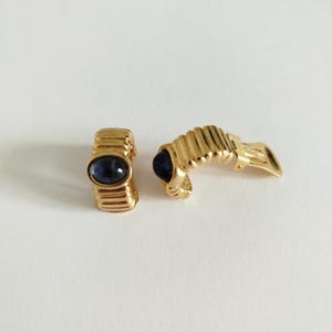 K&ouml;nnte beinhalten: Ein Paar goldfarbene Creolen mit einem dunkelblauen, ovalen Stein, der in jeden Reifen eingefasst ist.