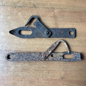 Puede incluir: Dos ganchos de metal oxidados con un gancho en un extremo y un extremo puntiagudo en el otro. Los ganchos están en posición cerrada.