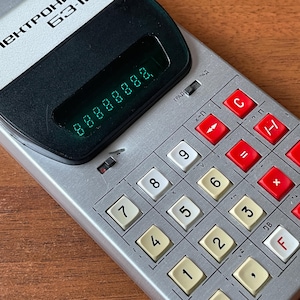 May include: Close-up of a vintage silver calculator with a black display showing the number 88888888. The calculator has white and red buttons with numbers and symbols. The word "Пектрон" is visible on the top left.
